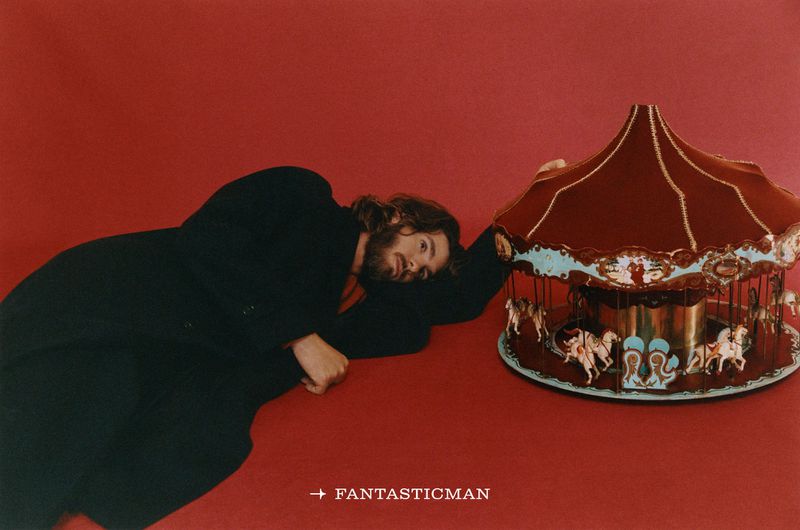 Actor Andrew Garfield lying on a red background next to a miniature carousel prop