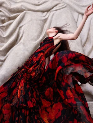 Model in red and black floral dress leaning against sculptural textured stone relief background