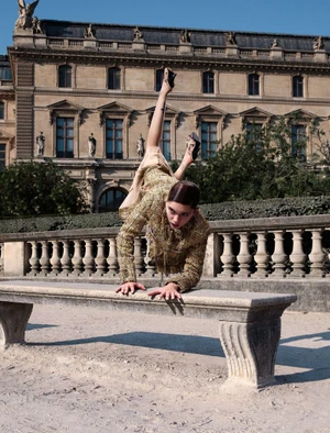 Model doing a handstand on a stone bench in front of a classical building exterior wearing a patterned jacket.