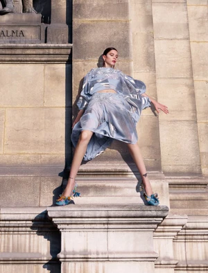 Model posing dramatically in a metallic blue two-piece outfit against classical stone architecture