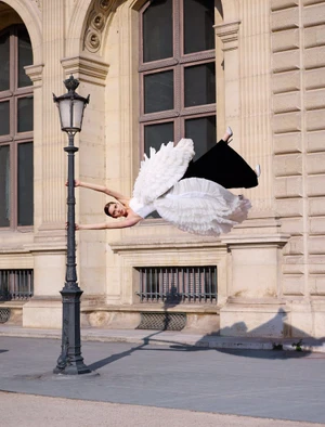 Model clinging horizontally to a black lamppost wearing a white ruffled dress for ICON Magazin Germany