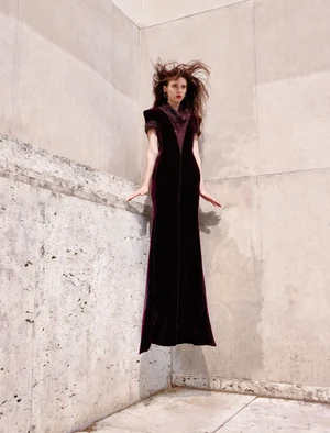 Model in a long burgundy velvet dress levitating against a concrete architectural wall for an editorial shoot.