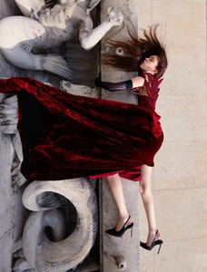 Model in red velvet gown and black heels posing dramatically against ornate stone sculptures for ICON Magazin Germany.