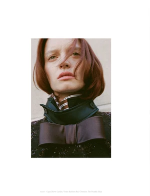 Portrait of a model with short red hair wearing a dark high-collared jacket and bow