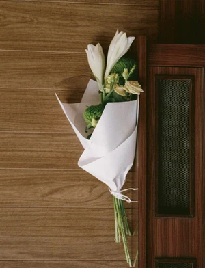 Bouquet of white lilies and greenery wrapped in white paper against wood panels