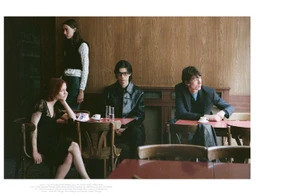 Four models seated and standing inside a wood-paneled cafe setting in an editorial fashion photograph.