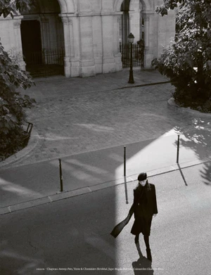 High-angle black and white photograph of a model walking on a cobblestone street near classical architecture.