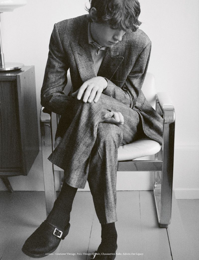 Young man in a tweed suit seated on a chrome chair in a minimal room