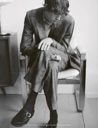 Young man in a tweed suit seated on a chrome chair in a minimal room