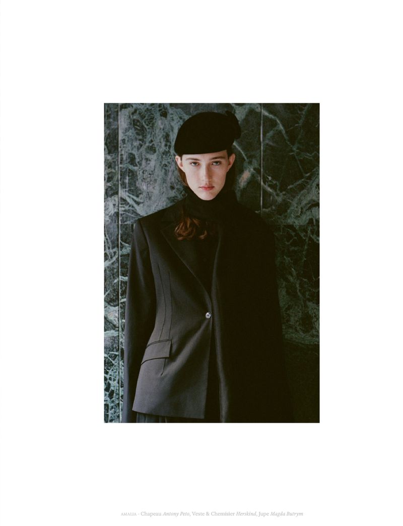 Model wearing a black blazer and beret standing against a dark marble wall in an editorial portrait for Coeur Magazine.