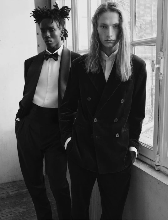 Black and white portrait of two male models in tailored eveningwear standing by a window for V Man by photographer Alvaro Beamud Cortes.
