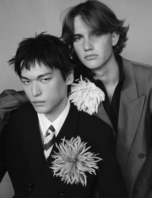 Two male models wearing tailored suits with large flower brooches in a portrait by photographer Alvaro Beamud Cortes for V Man.