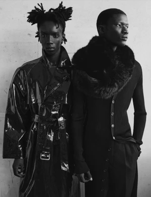 Two male models in black autumn fashion standing against a plain background in a monochrome studio portrait.