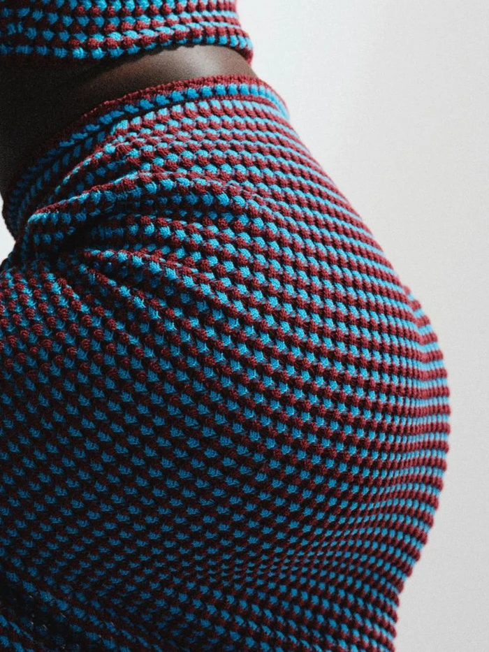 Close-up of a model wearing a textured knitted two-piece outfit in blue and burgundy against a plain light background.