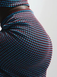 Close-up of a model wearing a textured knitted two-piece outfit in blue and burgundy against a plain light background.