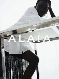 Model Athiec Geng wearing a white shirt and black fringe skirt leaning on a chrome table for Alaïa