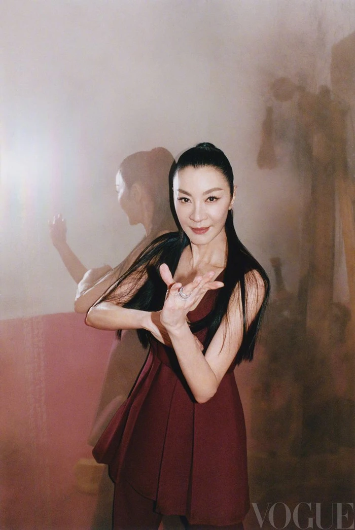 Michelle Yeoh in a burgundy dress with dark hair tied back in a half-up style poses against a textured background for Vogue China.