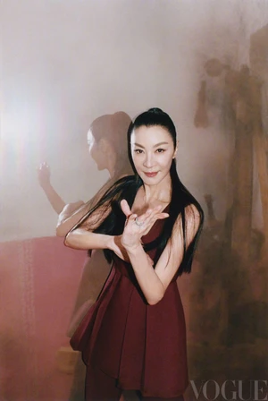 Michelle Yeoh in a burgundy dress with dark hair tied back in a half-up style poses against a textured background for Vogue China.