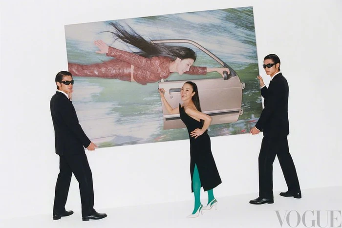 Michelle Yeoh in a black dress and two men in suits hold a large framed photograph against a white background.