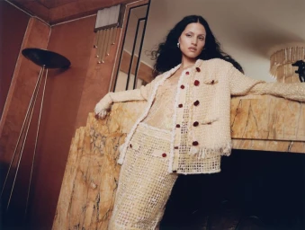 Gabbriette wearing a textured cream jacket and skirt leaning against a marble fireplace in an editorial shoot for Vogue Mexico