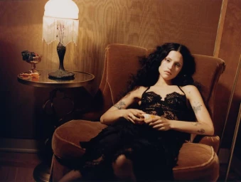 Model Gabbriette seated in a brown velvet armchair wearing black lace lingerie for Vogue Mexico editorial.