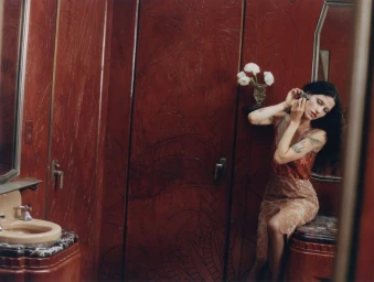 Model Gabbriette posing in a monochromatic deep red interior wearing lace clothing, adjusting her earring in front of a mirror.