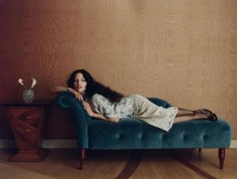 Model Gabbriette lounging on a tufted teal velvet chaise lounge against a warm wooden panel wall for Vogue Mexico.