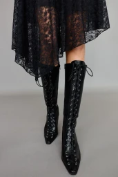 Close-up of black lace-up knee-high boots and a black lace dress against a plain grey seamless background.