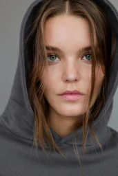 Close-up portrait of a woman wearing a dark grey hoodie against a neutral background