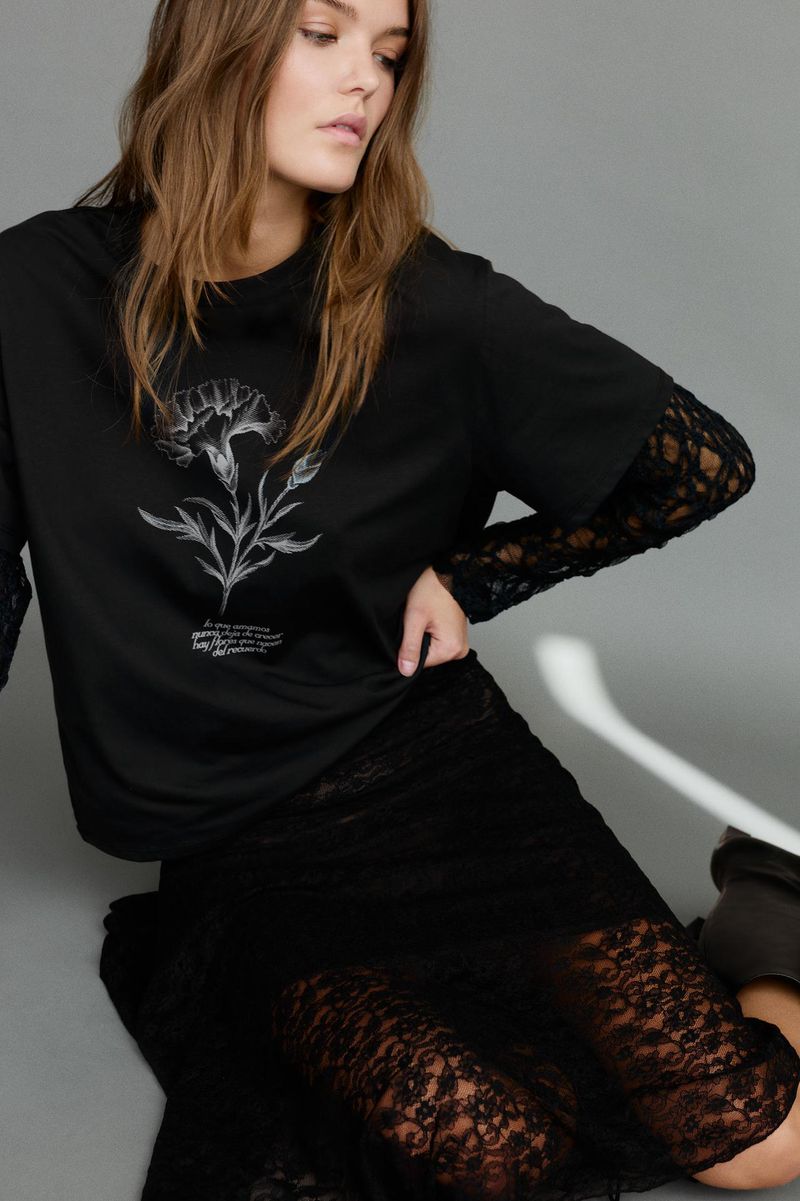 Model wearing a black t-shirt with a white floral print and black lace skirt against a plain grey studio backdrop