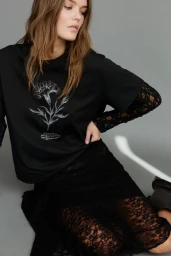 Model wearing a black t-shirt with a white floral print and black lace skirt against a plain grey studio backdrop