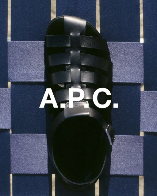 Close-up of a black leather gladiator sandal from A.P.C. displayed on a blue woven surface, showcasing its textures and design.