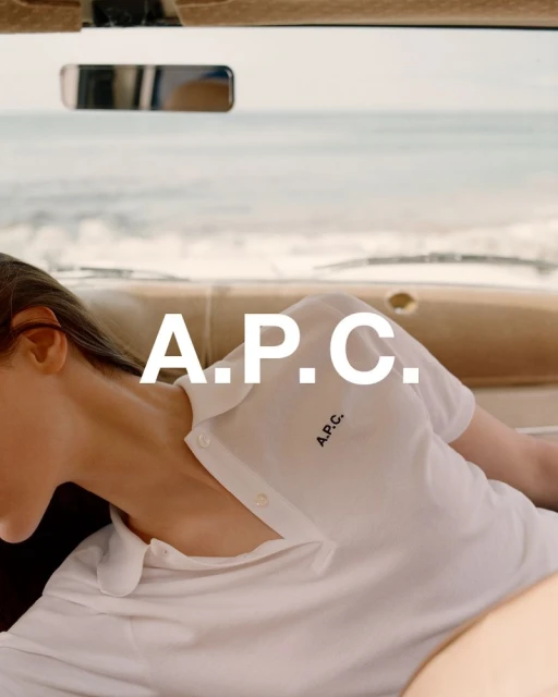 Woman in a white polo shirt lies inside a car with a cream-colored interior and an ocean view, featuring the APC logo and branding.