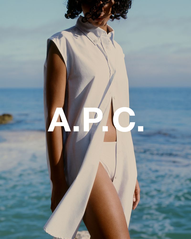 An adult female posing in a striped button-down dress against a sea backdrop, emphasizing fashion and the natural environment.