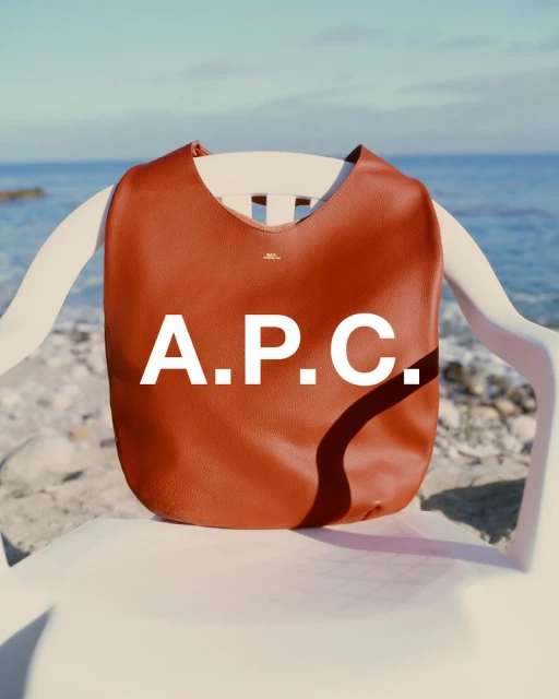 Brown leather tote bag with the APC logo displayed on a white plastic chair with a beach and ocean in the background.