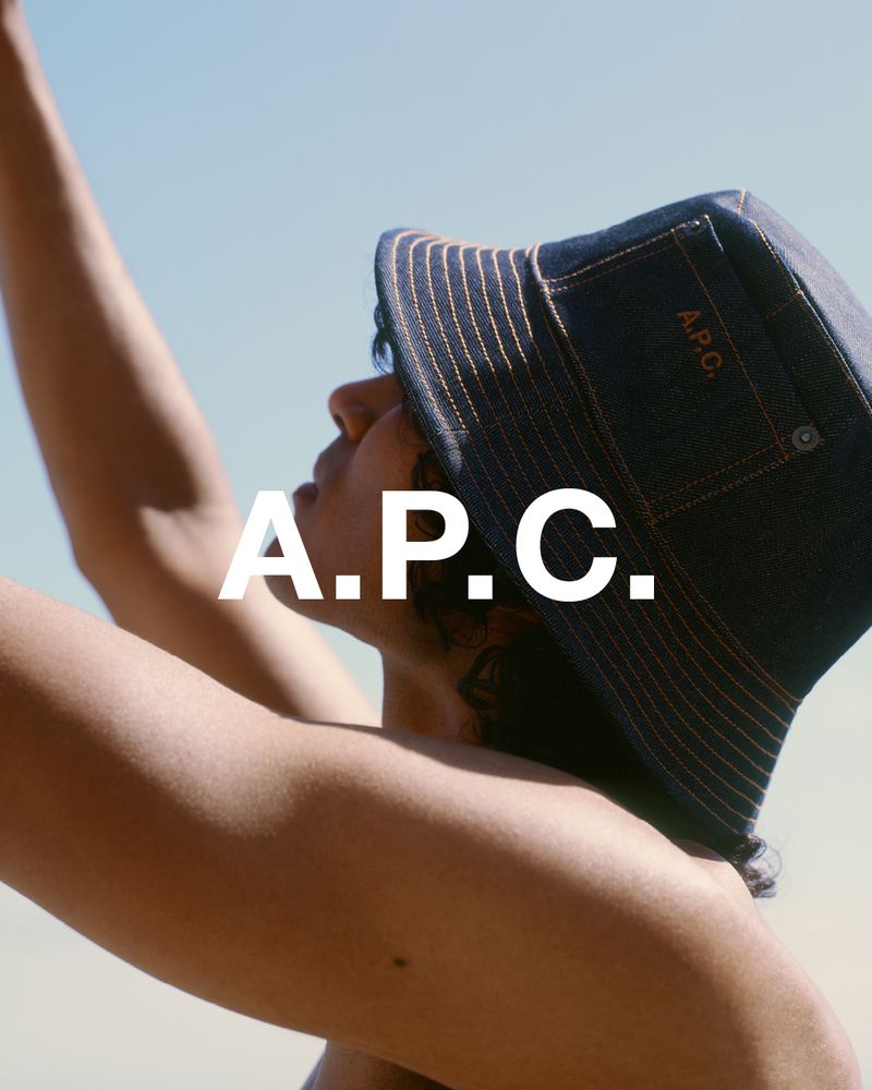 Denim bucket hat with A.P.C. logo on an adult with a tan skin tone, gazing toward the sky in an outdoor setting with natural lighting.