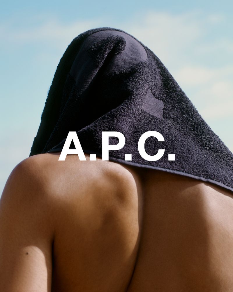 Close-up shot featuring an adult with a black towel draped over their head, set against a bright sky and featuring the text “A.P.C.”