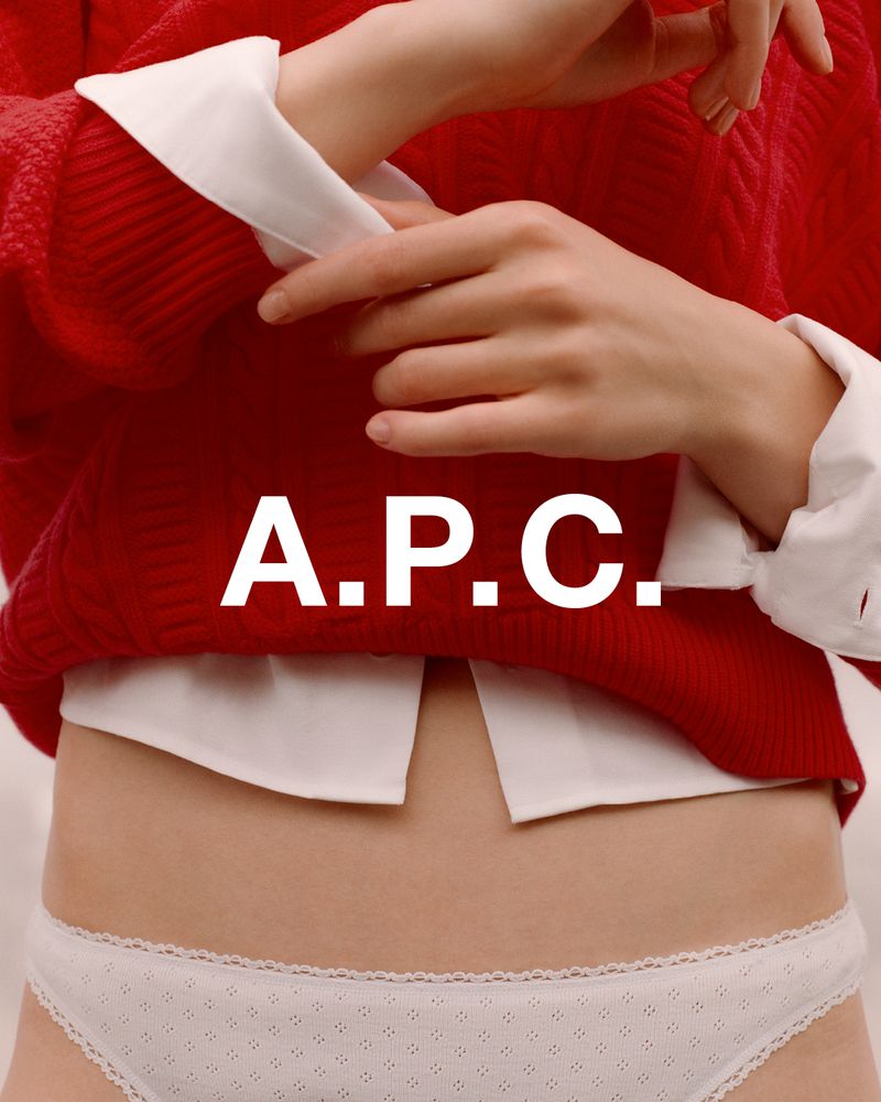 Fashion shot: woman in red sweater and white button-down shirt with visible stomach and white underwear posing in a light studio.