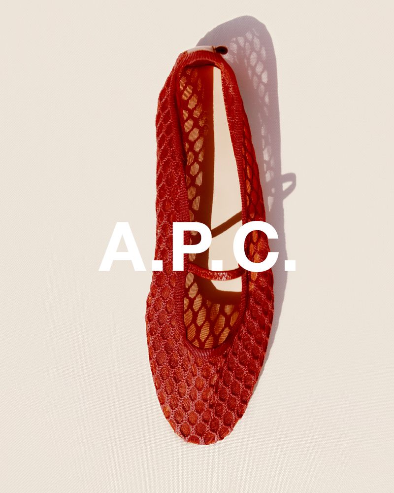 Close-up shot of a red ballet flat shoe with a woven design on a light beige background, casting a shadow on the surface.