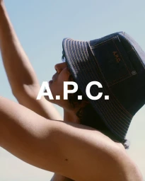 Low-angle profile of a person wearing a dark denim bucket hat with orange stitching against a clear pale blue sky.