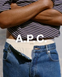 Close-up of a person wearing blue denim jeans and an off-white waistband under a navy striped knit with crossed arms.