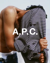 A shirtless man holding a striped navy and white sweater up against his face for the A.P.C. Summer 2025 campaign.