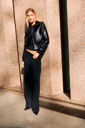 Model leaning against a pink granite pillar wearing a black leather jacket and black trousers for Pull&Bear.