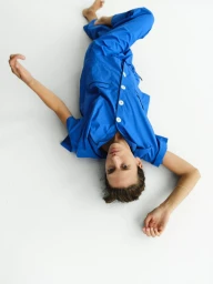 Model lying on a plain white floor wearing a bright blue pajama set with white buttons.