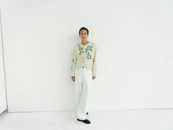 Model standing against a plain white background wearing an off-white embroidered jacket and white trousers