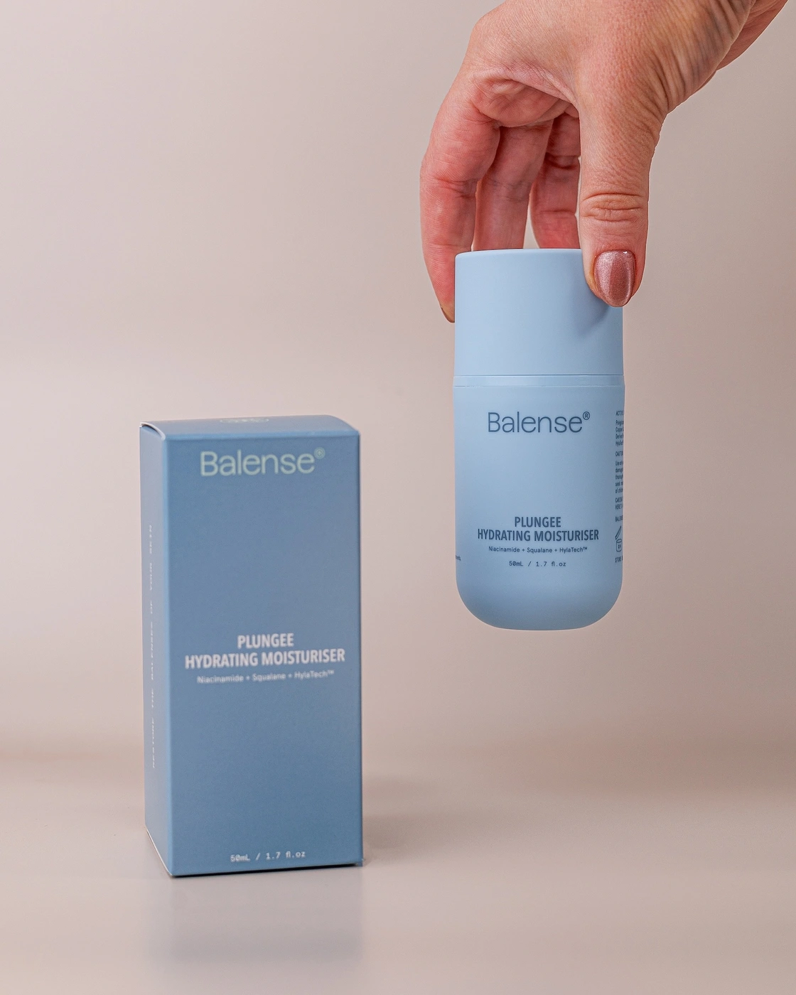 Hand holding a light blue Balense hydrating moisturiser bottle beside its matching carton on a neutral background