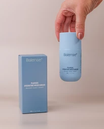 Hand holding a light blue Balense hydrating moisturiser bottle beside its matching carton on a neutral background