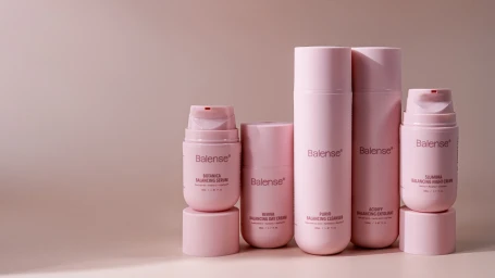 Five pink Balense skincare bottles and pump dispensers arranged neatly on a smooth pale surface against a soft neutral background.