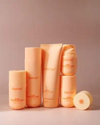 Arrangement of peach-colored Balense skincare bottles and tubes standing upright on a matching neutral surface.