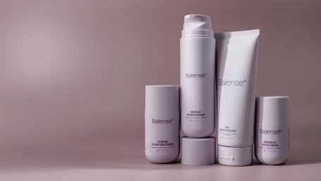 Four Balense skincare bottles and tubes arranged on a muted pink surface with soft studio lighting